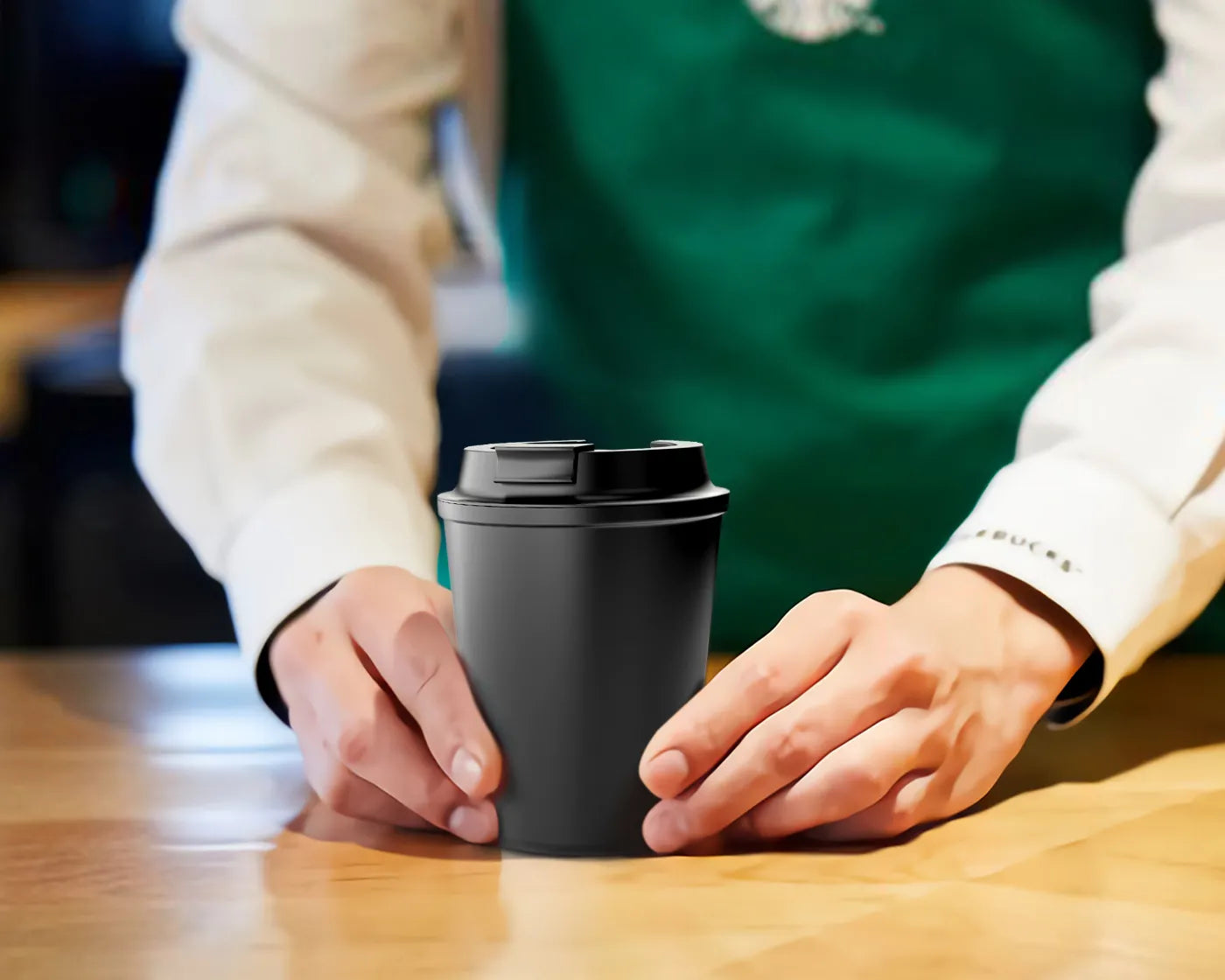 Barista presenting a matte black coffee cup at Starbucks, highlighting brand's move to reusable containers.